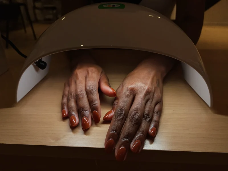 Illustration af hænder med blank terracottabrun gel under en lille neglelampe